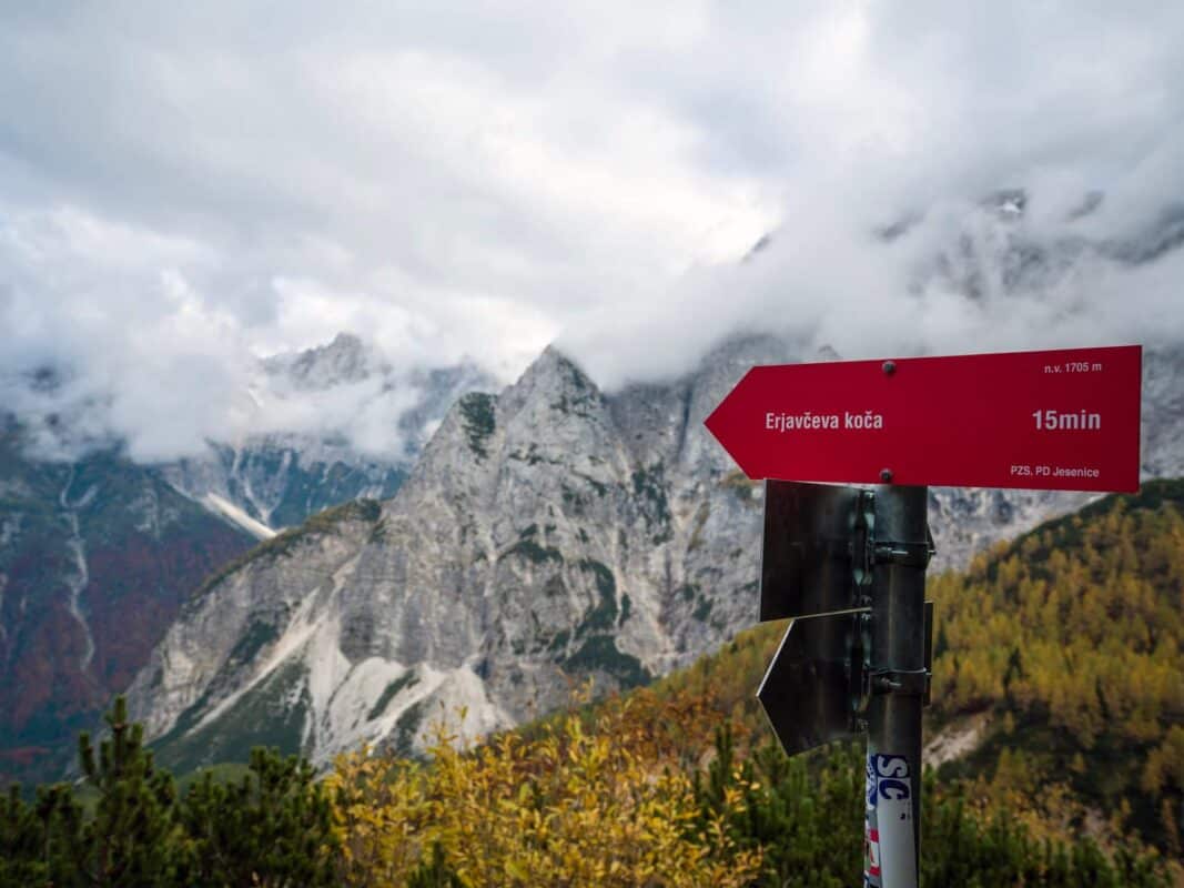 Abgelegene Berglandschaft mit nebelumhüllten Felsgipfeln und herbstlich gefärbten Bäumen bei der Erjavčeva-Hütte.